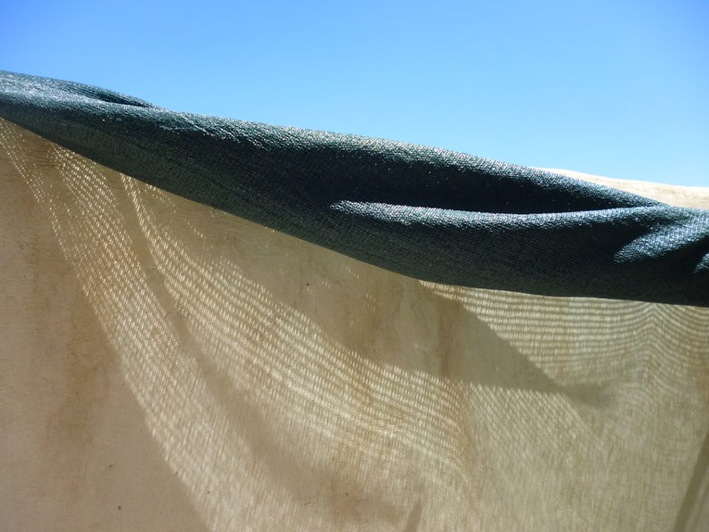 Close-up view of hands setting up a portable fabric windscreen barrier next to an RV campsite, with a fire ring visible in th