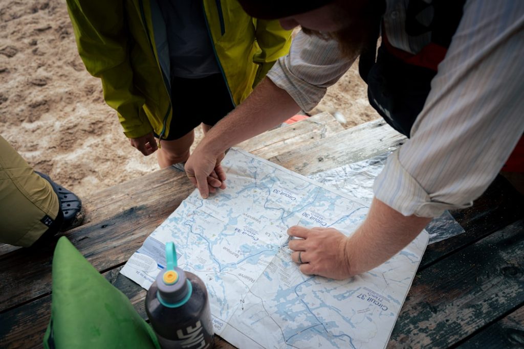 Show an RV camper walking through a campground with a site map in hand, evaluating different empty campsites. In the backgrou