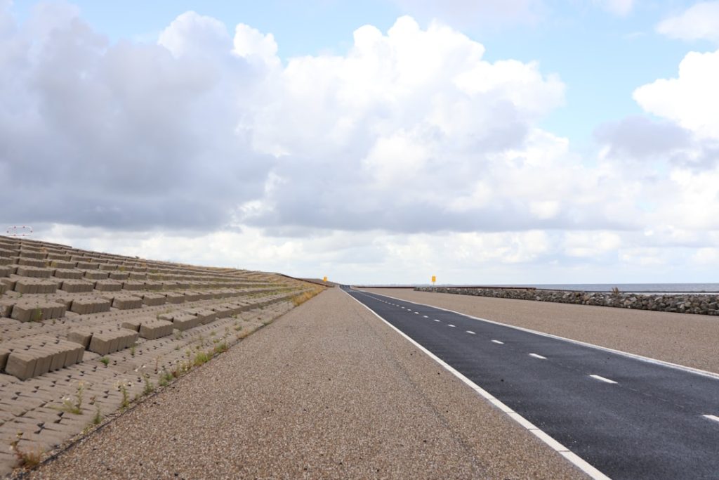 Show an RV driving on an open highway with strong crosswinds visibly affecting it - perhaps leaning slightly or with dust/deb