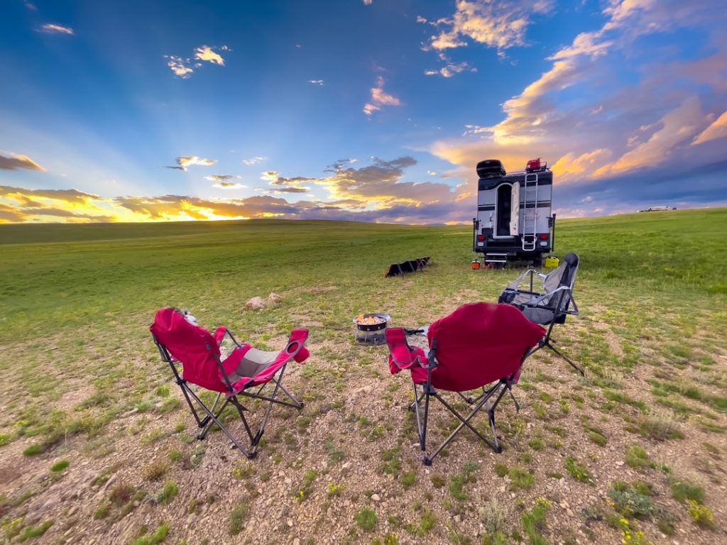 Show an RV campsite during golden hour with camp chairs positioned facing west toward the sunset, with RVers from neighboring