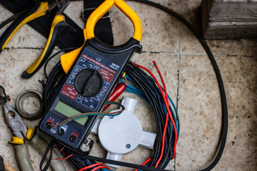 Close-up view of hands using a digital multimeter with amp clamp attachment around wires leading to an RV leveling jack motor