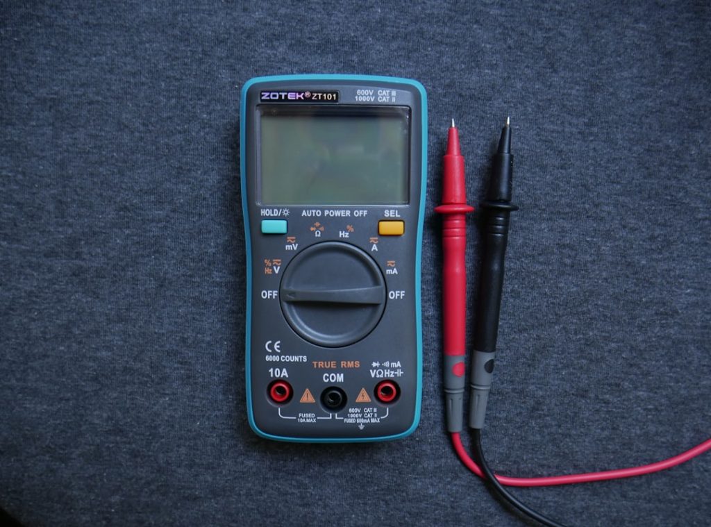 Close-up shot of hands using a digital multimeter to test a small thermistor sensor probe inside an RV refrigerator cooling u