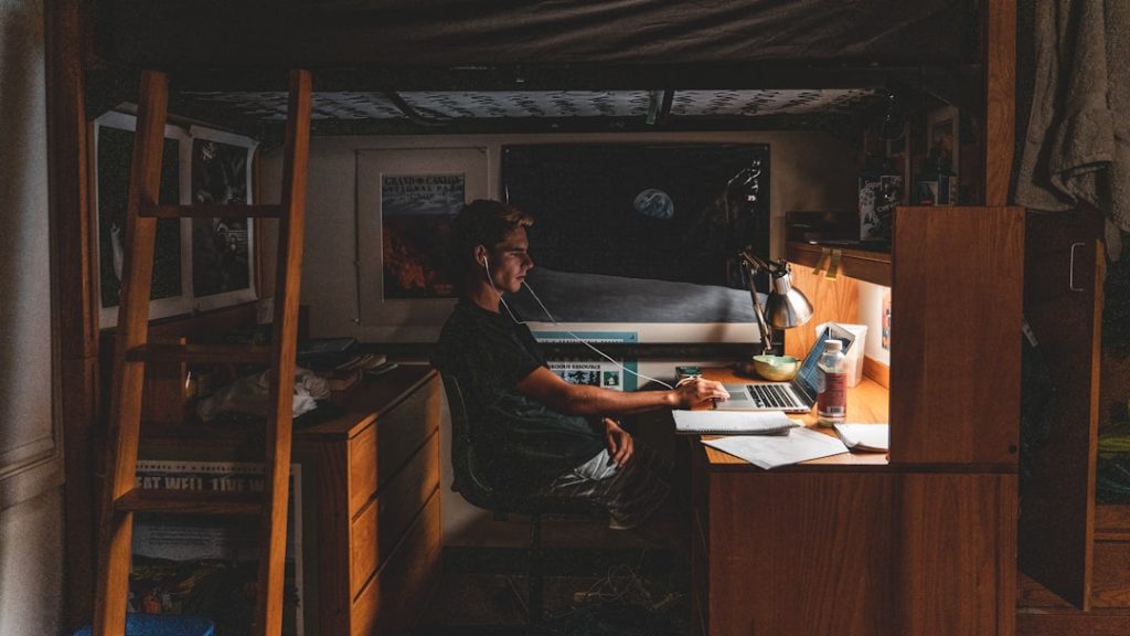 Close-up view of someone working on a laptop inside an RV with a large public library visible through the window in the backg