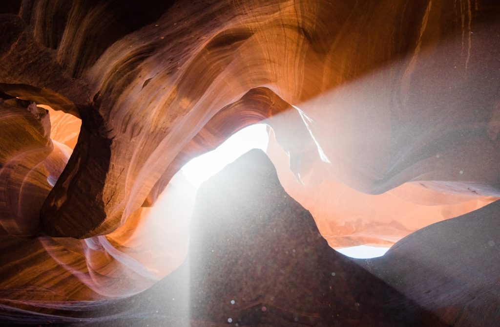Golden sunlight streaming through Upper Antelope Canyon's narrow opening, illuminating layered purple and orange sandstone walls